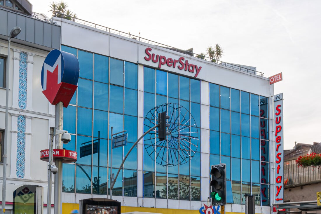 Cam cepheli binada kırmızı SuperStay tabelası, önünde tramvay durağı